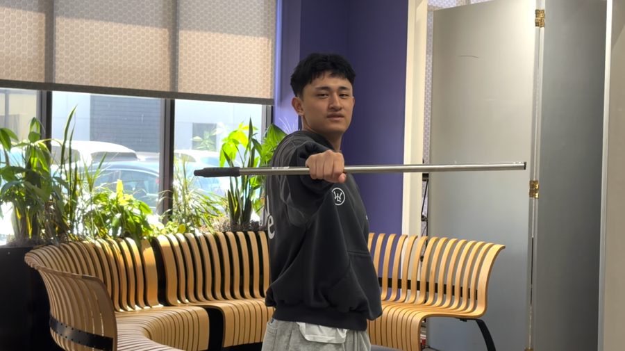 The creator holding a straight metal staff toward the camera in an office.
